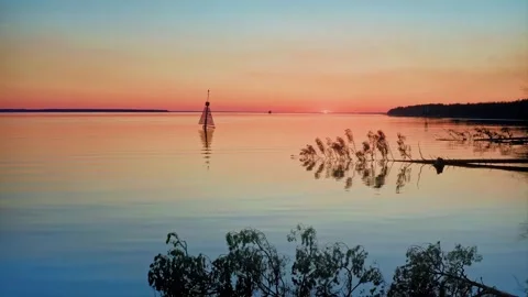 Vibrant Colors Dance on Gentle Waves, Fallen Trees, and a Silent Lighthouse Stock Footage 257777358