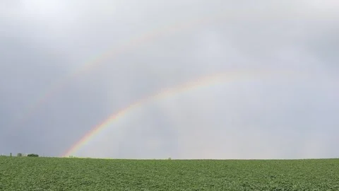 A vibrant double rainbow arching over a green field Stock Footage 296827648