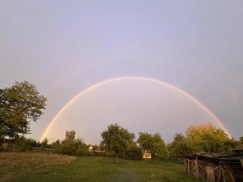 Vibrant double rainbow arching over a rural countryside landscape at sunset Foto stock