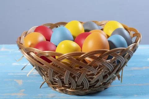 Vibrant dyed Easter eggs in a woven wicker basket on a rustic blue wooden t.. Stock Photos