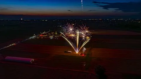Vibrant Fireworks Exploding In The Night Sky Over A Farm With A Distant Cro.. Stock Photos
