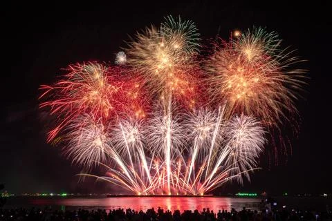 Vibrant Fireworks Exploding Over Dark Reflective Sea With Spectators Watchi.. 库存照片