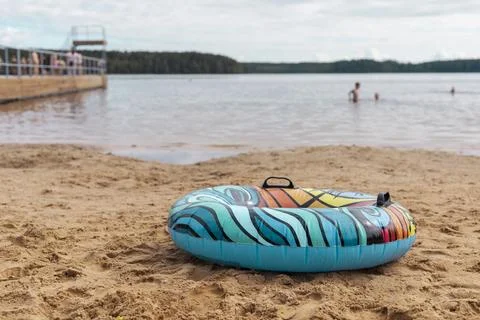 A vibrant float ring rests on the sandy shore near a lake. In the background, Stock Photos