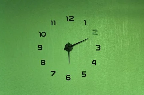A vibrant green clock on a textured wall with black hands. Stock Photos