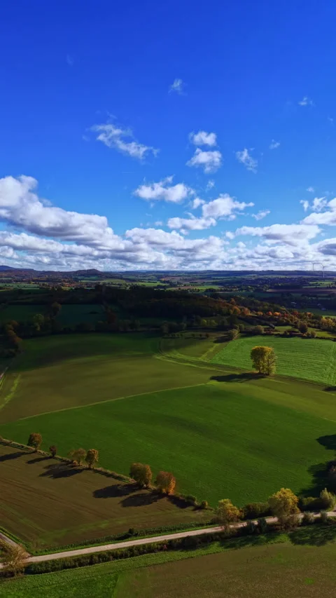 Vibrant green landscape under a clear blue sky with fluffy clouds and rolling Stock Footage 331260753