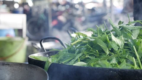 Vibrant greens are flash-cooked in a wok over high flames at a street market Stock Footage 314119712