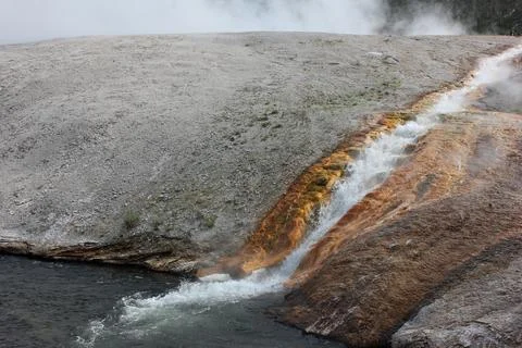 Vibrant hot spring flows into clear water in geothermal landscape during a .. Stock Photos
