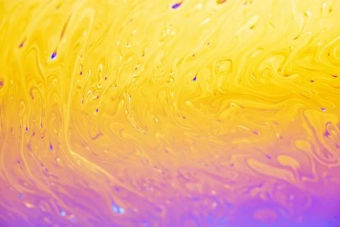 Vibrant iridescent soap bubble surface with swirling yellow and purple patter 스톡 사진
