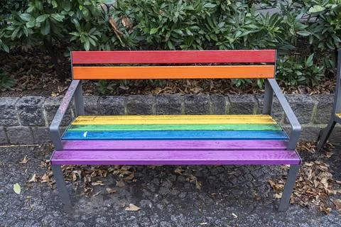 A vibrant, multicolored bench featuring rainbow stripes, placed outdoors amidst Stock-Fotos
