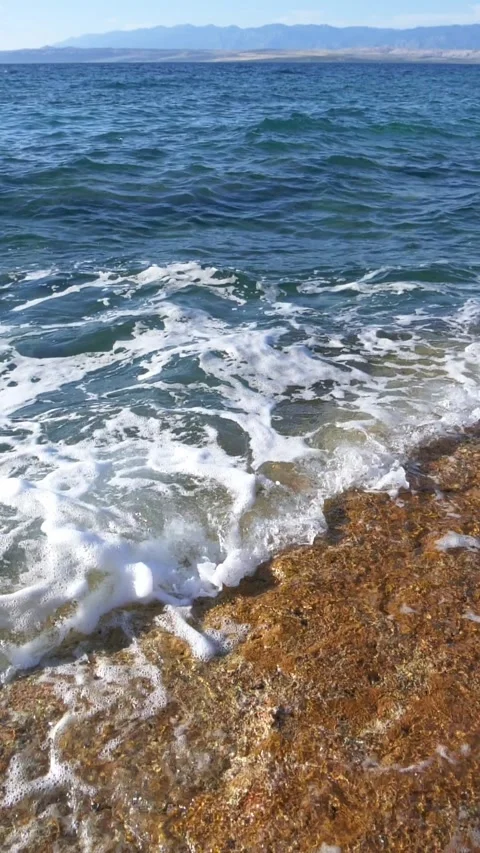 Vibrant ocean waves crash dynamically onto the wet rocky shoreline Stock Footage 337414587