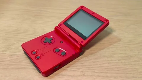 Vibrant old red portable handheld video gaming console on a wooden table, Video stock 318310934