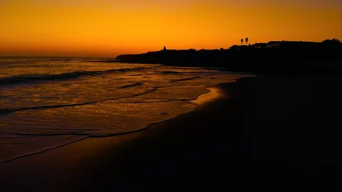Vibrant orange sky over dark waves on California Beach Town, fly over Stock Footage 129738938