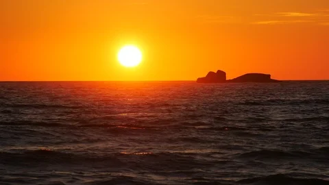 Vibrant orange sky at sunset on ocean with rocky island in silhouette Stock Footage 110619765