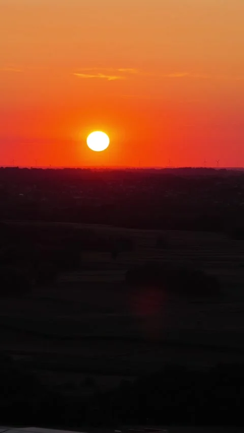 Vibrant orange sun setting over a silhouetted rural landscape and wind turbines 스톡 동영상 347883205