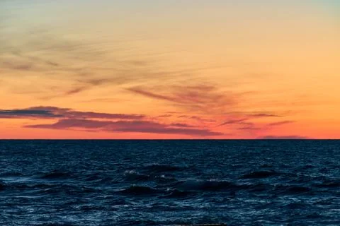 Vibrant orange sunset over restless ocean waves with soft cloud patterns Stock Photos