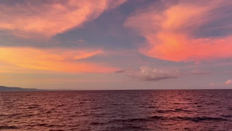 Vibrant orange yellow sunset over sea with boat wake in foreground, dark clouds Video stock 325514000