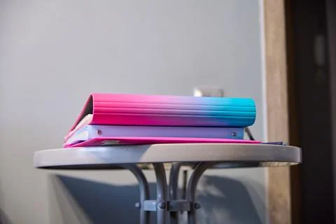 Vibrant pink and blue gradient binder on round metal table in soft indoor l.. Foto stock