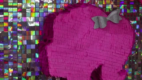 Vibrant pink piñata with silver bow against shiny sequin backdrop and pink Stock Footage 283635385
