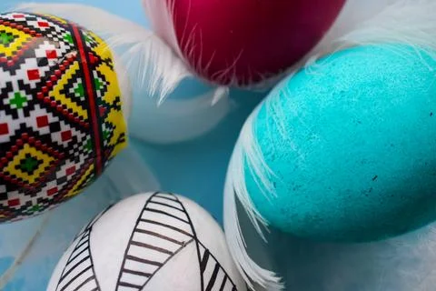 Vibrant Pysanka and Dyed Easter Eggs with Soft Feathers on Blue Background Stock Photos