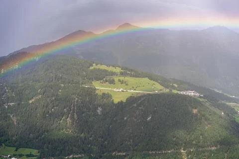Vibrant Rainbow Arching Over Green Mountain Valley and Alpine Village Landsca Stock Photos