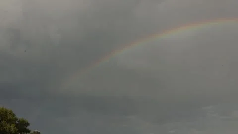 Vibrant rainbow arcs across a dramatic, cloudy sky after a storm Stock Footage 337129442