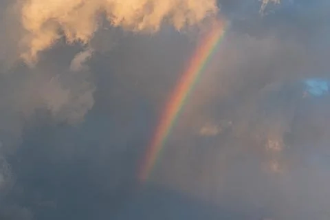 Vibrant rainbow arcs over dense, layered clouds from one side to another, cas Stock Photos
