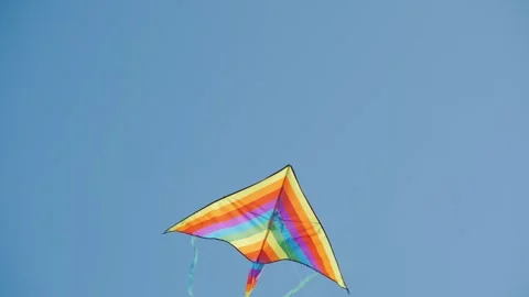 A vibrant rainbow-colored kite soars gracefully against a clear blue sky, f.. Stock Footage 334652593
