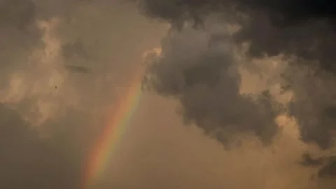 Vibrant rainbow fragment cutting through storm clouds during a dramatic evening  Stock Footage 346679494