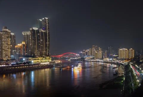 A vibrant red arch bridge spans a tranquil, foggy river framed by a multi-l.. Stock Photos