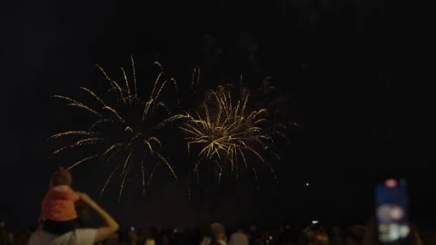 Vibrant red fireworks bursting over a silhouetted crowd at night Stock Footage 334590382