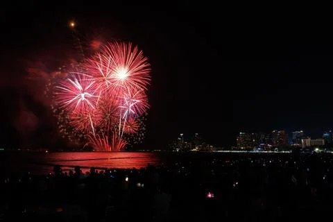 Vibrant Red Fireworks Exploding Over Coastal City Skyline At Night Wide Shot Stock Photos