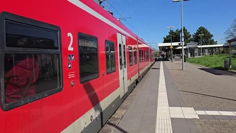 A vibrant red passenger train waits at a sunny outdoor station platform u.. Stock Footage 341878626