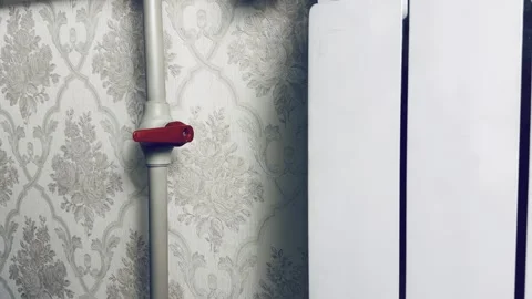 Vibrant red radiator valve on gray pipe against ornate floral wallpaper in cozy  Stock Footage 327637304