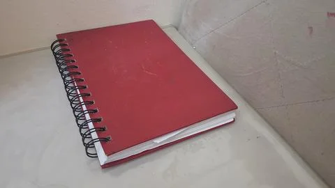 Vibrant red spiral notebook rests on a clean light desk surface Stock Photos