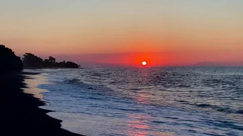 Vibrant Red Sun Setting Over Ocean Waves on Beach in Bali 스톡 사진