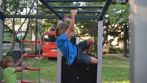 A vibrant scene of two children playing on outdoor gym equipment. One climbs a Stock Footage 285179902