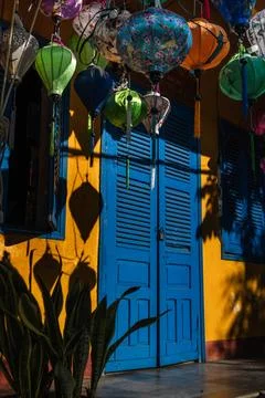 Vibrant silk lanterns hanging in front of a bright blue door on a yellow Fotos de archivo