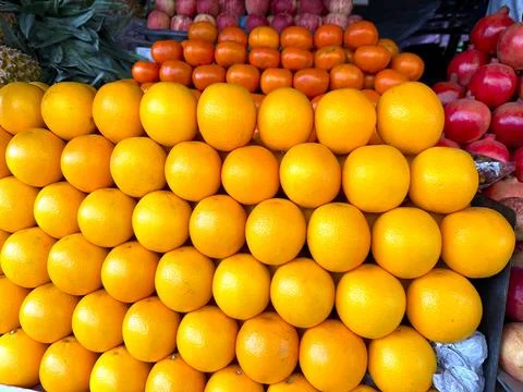 A vibrant stack of fresh oranges rests alongside tangerines, apples and pomeg Stock-Fotos
