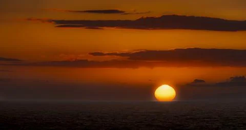 Vibrant sunset over the ocean with dramatic clouds and glowing sun disk Photos