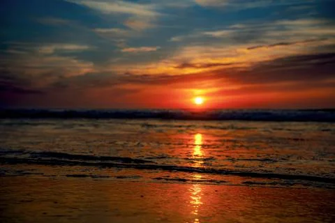 Vibrant sunset over the ocean with dramatic clouds and reflections on wet san Foto stock