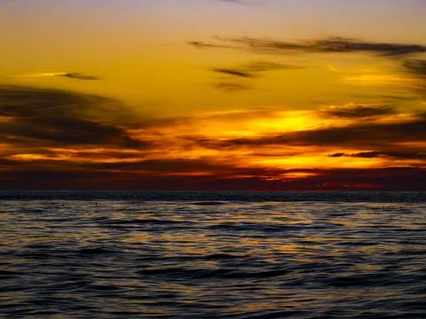 Vibrant sunset over the ocean with dramatic clouds and rippling water Stock Photos