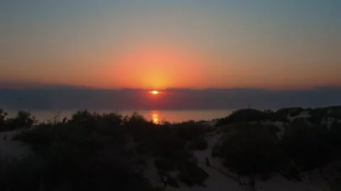 Vibrant sunset over ocean with sun reflecting on water. People walk on paths Stock Footage 320606040