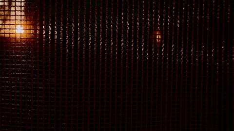 Vibrant sunset rays piercing dark chain link fence mesh in urban twilight e.. Stock Photos