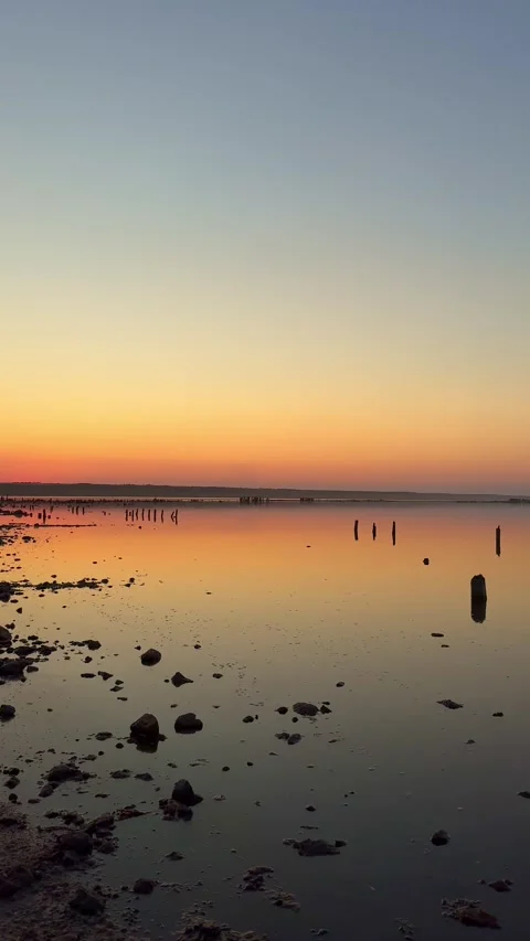 Vibrant sunset reflection on calm salt lake with wooden piles Stock Footage 341745274