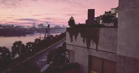 Vibrant sunset reflects on calm river with modern architecture nearby Ilustración de archivo