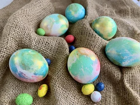 Vibrantly painted Easter eggs of various sizes are displayed on a burlap cloth, Stock Photos