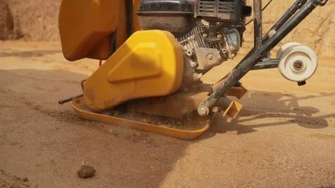 Vibrating plate compactor compacting soil for construction groundwork Stock Photos