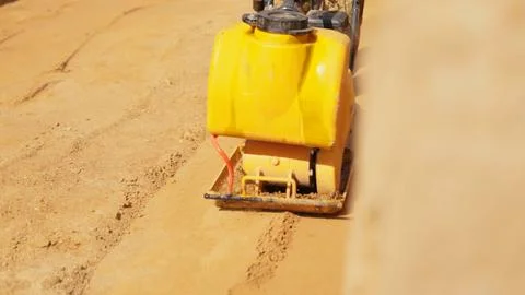 Vibrating plate compactor consolidating sand on construction site Stock Photos