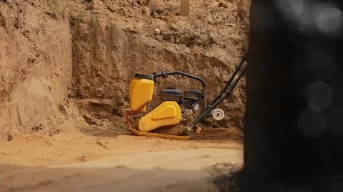 Vibrating plate compactor consolidating soil at construction site 스톡 사진