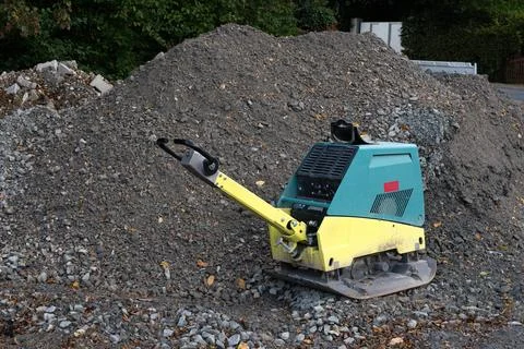 Vibratory plate compactor on a construction site next to a pile of gravel. Stock Photos